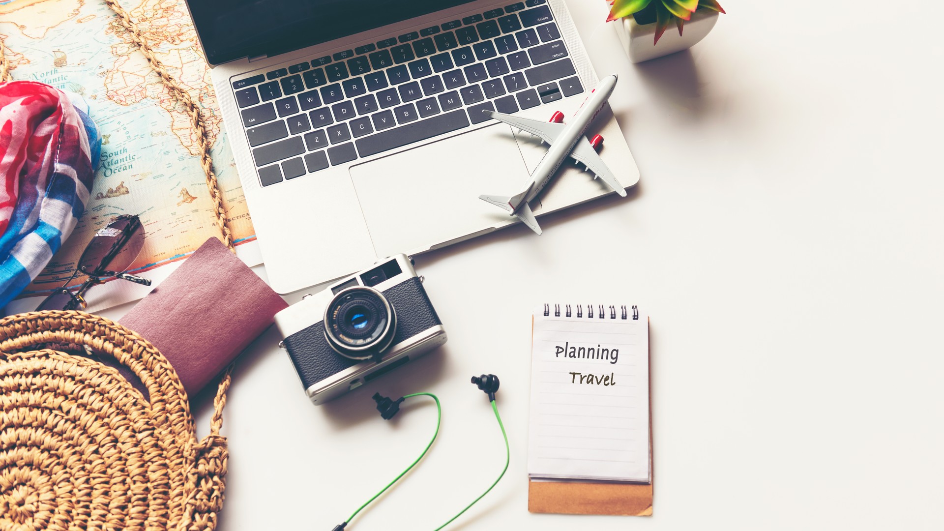 Traveler planning vacation trip and searching information or booking hotel on laptop with accessories item women and map, old camera.  Top view and white background